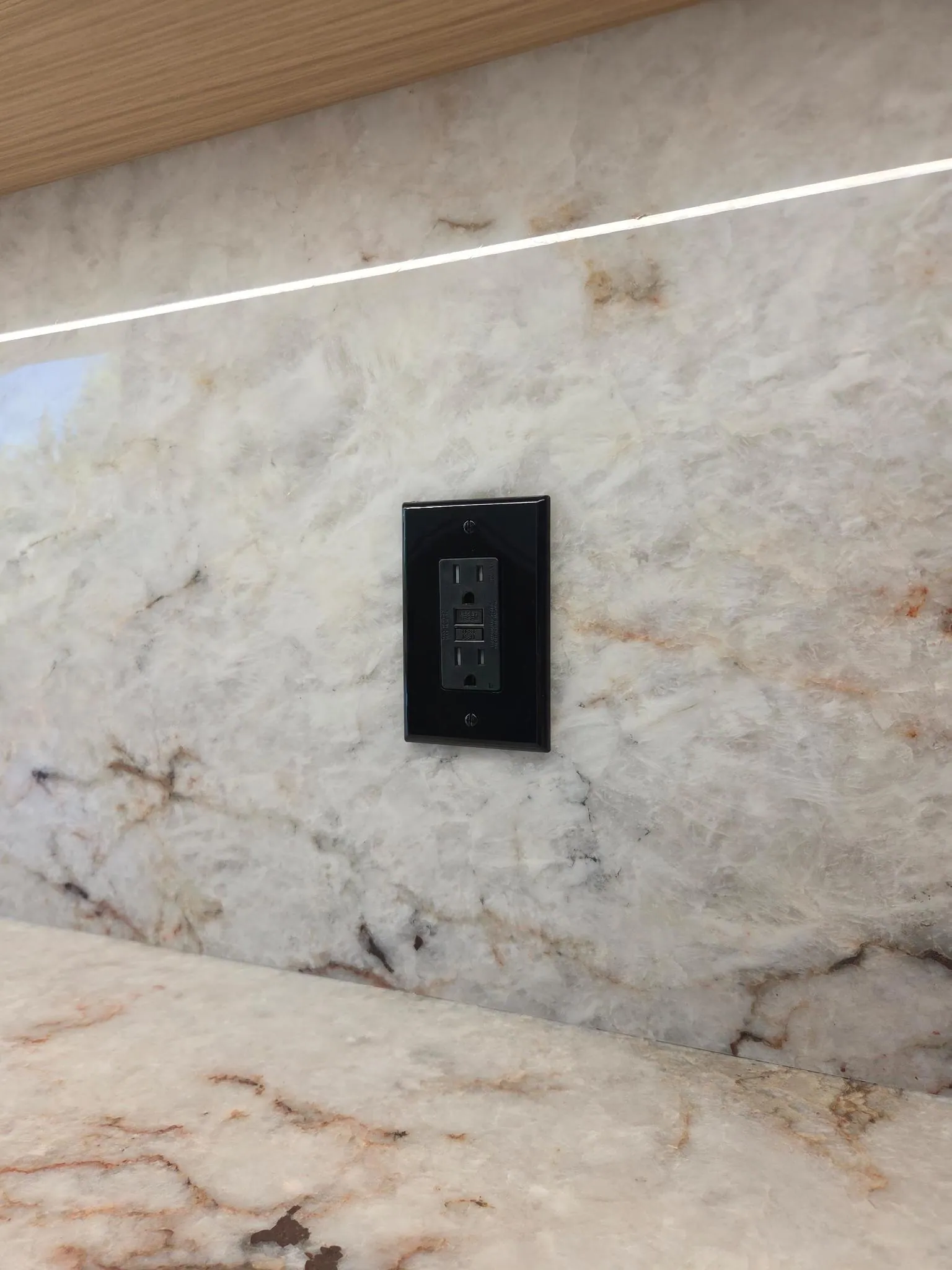 Black GFCI receptacle installed in a finished stone backsplash