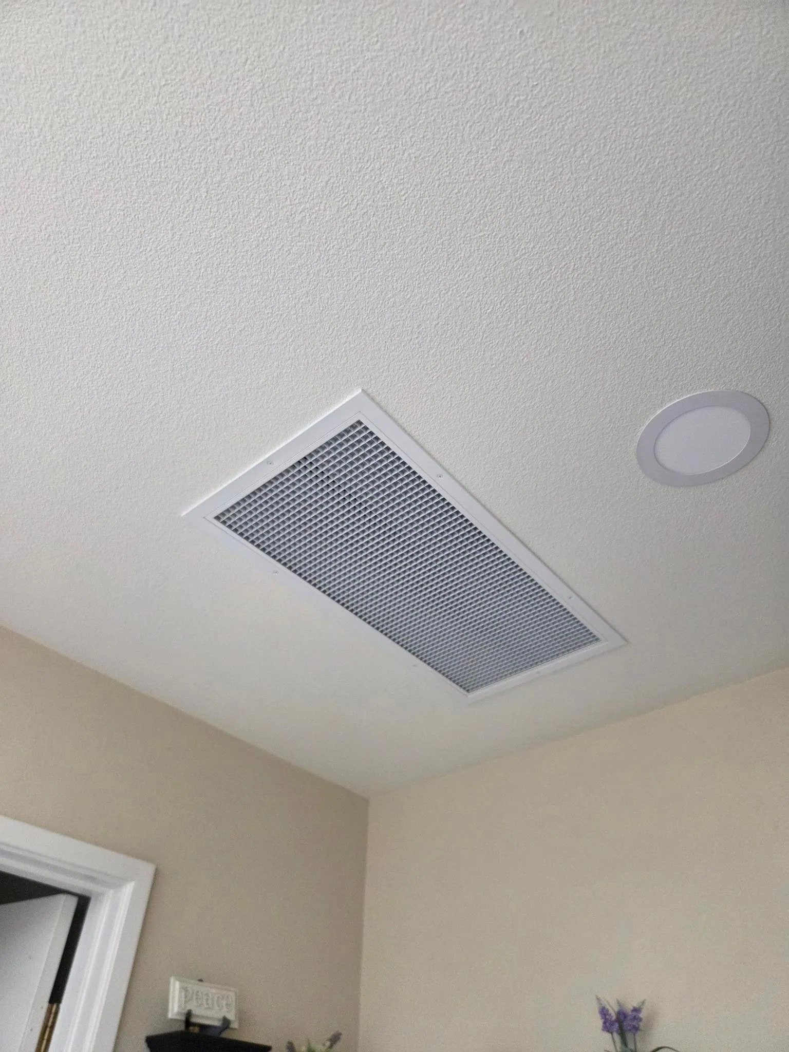 Whole-house fan grille installed beside a recessed ceiling light